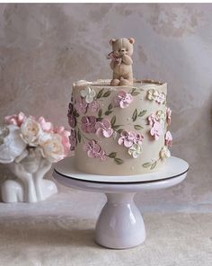 a white cake with pink flowers and a teddy bear on top