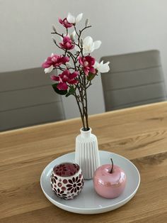 a white plate topped with two donuts next to a vase filled with pink and white flowers