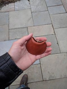 a hand holding a small brown wallet on top of a stone floor next to a person's foot