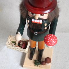 a nutcracker figurine holding a basket of mushrooms and an orange mushroom