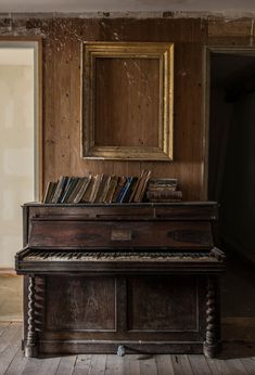 an old piano with books on it in front of a mirror and wooden paneled wall