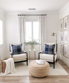 a living room with two chairs and a round ottoman in front of a window filled with pictures