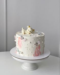 a white cake with pink and blue frosting on a plate next to a wall