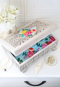 an ornate white box with flowers and jewelry on the table next to it is a flower vase