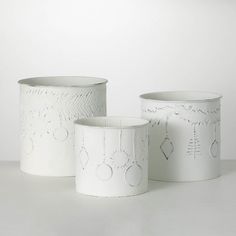 three white vases sitting next to each other on top of a table with designs