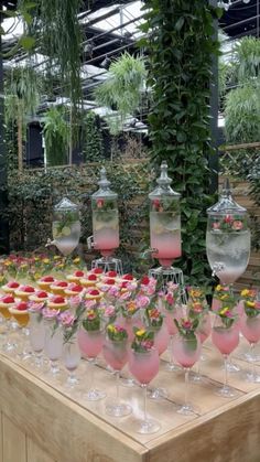 a table topped with lots of wine glasses filled with pink liquid and flowers in vases