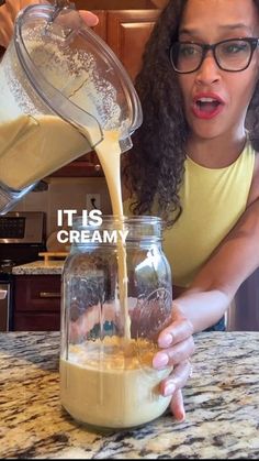 a woman pouring milk into a glass jar on top of a kitchen counter with the words it's creamy in front of her