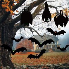 bats hanging from the branches of a tree in front of a house with pumpkins on it