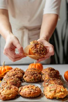 a person holding a piece of food in their hand over some muffins on a baking sheet