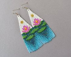 a pair of beaded earrings with pink flowers on top of water and green leaves