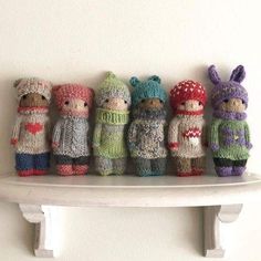 a row of knitted dolls sitting on top of a white shelf next to each other