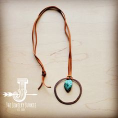 a necklace with a turquoise stone in the middle on a brown leather cord that is attached to a hook