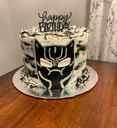 a black and white birthday cake sitting on top of a wooden table next to a window