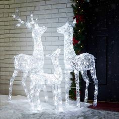 two lighted reindeer standing next to each other in front of a brick wall and door