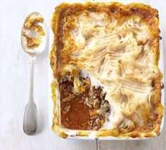 a casserole dish with meat and vegetables in it next to a spoon on a white table