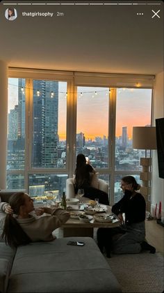 two women sitting on couches in front of large windows with city skyline behind them