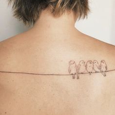 a woman's back with three birds on a wire tattooed on her left shoulder