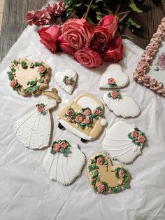 several decorated cookies sitting on top of a table next to red roses and pink flowers