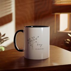 a white and black coffee mug sitting on top of a wooden table next to a plant