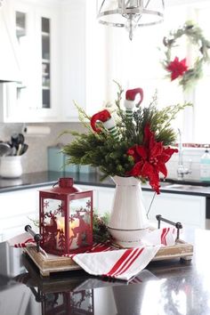 a christmas arrangement on a kitchen counter with red and green flowers in a white pitcher