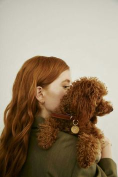 a woman with long red hair holding a brown poodle in her arms and kissing it's face