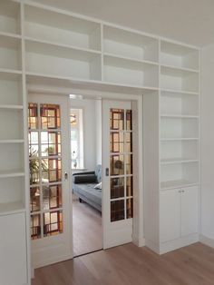 an empty living room with white bookcases and wood flooring is seen through the glass doors