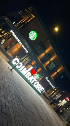 a starbucks sign on the side of a tall building at night with lights in the background