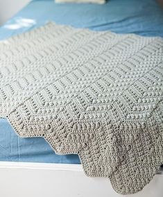 a crocheted blanket on top of a bed with blue sheets and white pillows