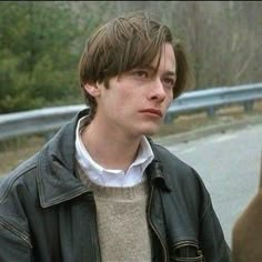 a young man standing on the side of a road next to a brown bear in front of him