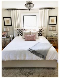 a white bed sitting in a bedroom next to a window with curtains and pillows on top of it