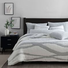 a bed with white and grey comforter in a bedroom next to a night stand