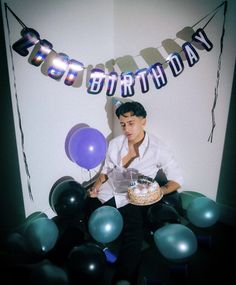 a man sitting in front of a birthday cake and balloons