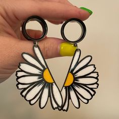 a pair of black and white earrings with yellow centers are held by a person's hand