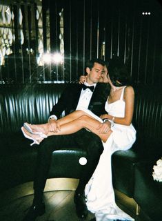 a man and woman are sitting on a black leather couch in a dimly lit room