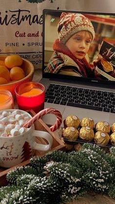 an open laptop computer sitting on top of a desk next to christmas decorations and candies