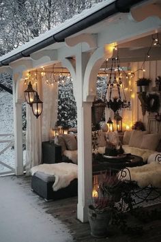 an outdoor covered porch with lights on the ceiling and furniture in the snow, surrounded by trees