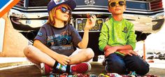 two young boys sitting on the ground next to a car