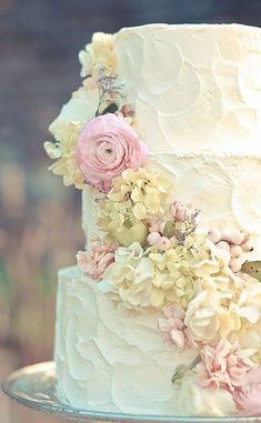 a wedding cake with white frosting and pink flowers on the top tier is sitting on a silver platter