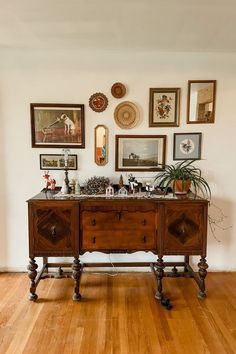 a wooden table sitting on top of a hard wood floor next to pictures and plants