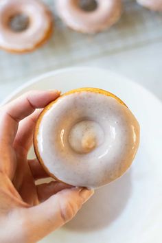 a person holding a glazed donut on a plate with other donuts in the background