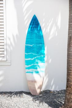 a blue surfboard sitting on top of a white wall next to a palm tree