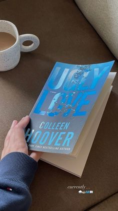 a person holding a book on top of a table next to a cup of coffee