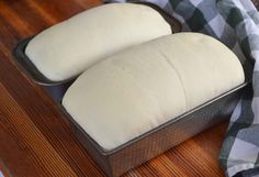 two loaves of bread sitting on top of a wooden table next to a checkered towel