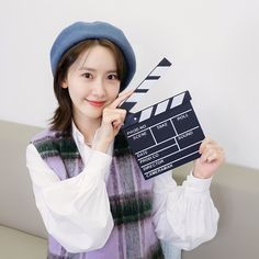 a woman holding up a clap board in front of her face and wearing a hat