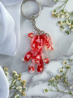 a red teddy bear keychain sitting on top of a marble table next to flowers