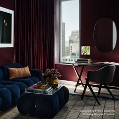 a living room with red walls and blue couch in front of a table, two framed pictures on the wall