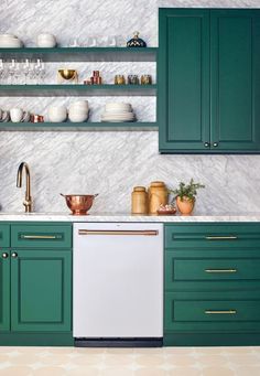 a kitchen with green cabinets and white marble counter tops, gold pulls on the dishwasher