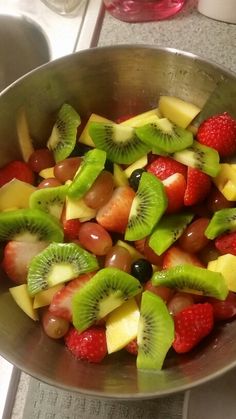 a metal bowl filled with sliced fruit on top of a counter next to a sink