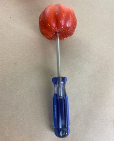 an orange and red pepper sitting on top of a blue plastic pepper grinder next to a tomato