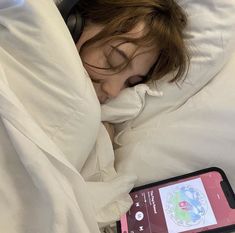 a woman is sleeping in bed with headphones on and an electronic device beside her